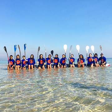 a group of poeople in a paddle board class hold up their paddles